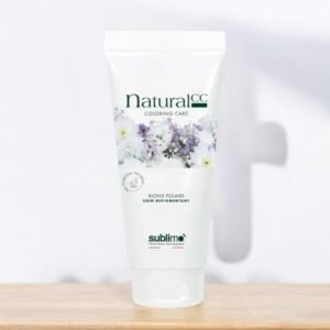 Un tube blanc de produit de soin capillaire Natural CC Coloring Care Blond Palaire est posé sur une surface en bois clair. Le tube présente des graphismes floraux et un texte vert. Le fond est blanc, légèrement flou, avec une pointe d'ombre. Le nom de la marque « Sublimo » figure en bas.