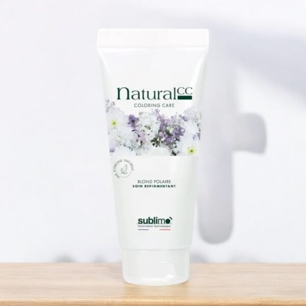 Un tube blanc de produit de soin capillaire Natural CC Coloring Care Blond Palaire est posé sur une surface en bois clair. Le tube présente des graphismes floraux et un texte vert. Le fond est blanc, légèrement flou, avec une pointe d'ombre. Le nom de la marque « Sublimo » figure en bas.