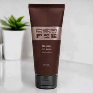 Un tube marron de 100 ml de Baume de Soin pour Cheveux Défi pour Homme est posé sur une surface blanche. Une plante verte floue est visible en arrière-plan.