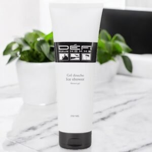 Un tube blanc de gel douche Défi pour Homme Ice Shower est posé sur une surface en marbre. Le tube est doté d'un bouchon noir et l'étiquette comporte des graphiques et du texte en noir et blanc. En arrière-plan, il y a des plantes vertes avec des pots blancs.