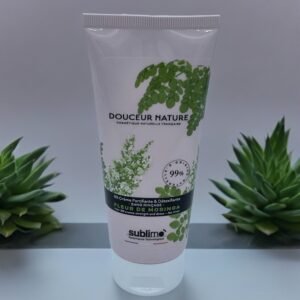 Un tube blanc de « BB crème capillaire Sublimo Fleur de Moringa 100 ml » avec une image de feuilles vertes sur l'étiquette. La crème est enrichie en fleur de moringa et prétend être d'origine naturelle à 99 %. Le tube est placé entre deux petites plantes succulentes sur une surface blanche sur fond gris.