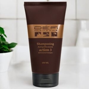 Un tube brun de shampoing antipelliculaire Défi pour Homme (Action 3), contenant 150 ml, est posé sur un comptoir de salle de bain blanc. Une plante à feuilles vertes est visible en arrière-plan.