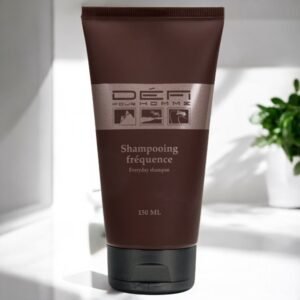 Un tube brun foncé de Shampooing Fréquence Cheveux et Corps-Défi pour Homme d'une contenance de 150 ml est étiqueté « Shampooing homme usage quotidien » et « Shampooing quotidien ». Le tube est posé sur une surface blanche, avec une plante verte floue en arrière-plan.