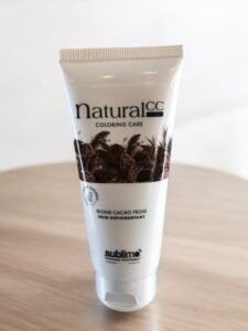 Un tube blanc de Sublimo Natural CC Color Care est posé sur une surface en bois. Le tube présente des images de fèves de cacao et l'inscription « Blond Cacao Froid, Soin Repigmentant ». Le design est épuré et minimaliste, avec une attention particulière portée aux ingrédients naturels.