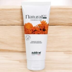 Un tube de produit capillaire Natural CC Coloring Care est présenté sur un fond en bois. Le tube présente des fleurs orange sur l'étiquette et indique « Orange Intense Soin Repigmentant ». Le nom de la marque « sublimo » est visible près du bas.