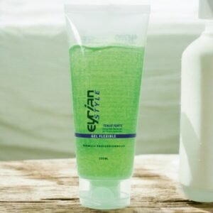 Un tube en plastique transparent étiqueté « Evrilan Style Gel Flexible » contient du gel vert et repose sur une surface en bois. Le tube a un texte bleu et vert et une capacité de 100 ml. Il y a une bouteille blanche partiellement visible en arrière-plan.