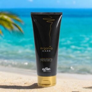 Un tube de masque onctueux Argania Care est posé sur une plage de sable avec une eau bleu clair et un palmier en arrière-plan. L'emballage noir et or élégant contraste avec le paysage naturel de la plage, suggérant luxe et détente.