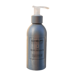 Un flacon pompe métallique portant la mention « Cire Texturisante-Défi Pour Homme-150 ml », sur lequel figurent les mentions « Fixation Normale » et « Fini Brillant Intense », repose sur un fond blanc uni, mettant en valeur le pouvoir coiffant raffiné de cette cire texturisante pour hommes.