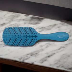 Une brosse à cheveux bleue, connue sous le nom de Brosse Biofriendly-bleu, au design ventilé, est posée sur un plan de travail en marbre. Le manche est doté d'une poignée texturée et d'un texte de marque près de la base, ce qui le rend à la fois élégant et respectueux de l'environnement pour un démêlage des cheveux sans effort.