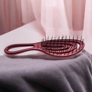 La Brosse Olivia Garden Rose, caractérisée par sa teinte rose et son manche courbé aux poils noirs, repose sur un tissu gris doux. Le fond est orné de rideaux rose clair, ajoutant à l'ambiance cosy et élégante.