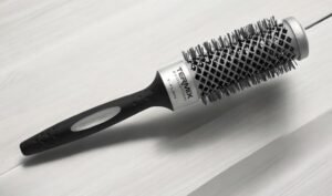 La Brosse Ronde Termix – Diam 37, une brosse à cheveux ronde avec un manche noir doté d'une poignée en caoutchouc et d'un corps argenté avec des poils, repose sur une surface claire.