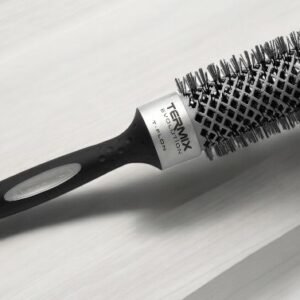 La Brosse Ronde Termix – Diam 37, une brosse à cheveux ronde avec un manche noir doté d'une poignée en caoutchouc et d'un corps argenté avec des poils, repose sur une surface claire.