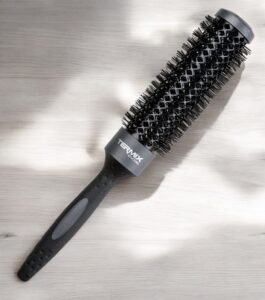 La Brosse Ronde XL Termix–Diamètre 60, dotée d’un design noir avec un manche texturé et des poils denses, repose sur une surface en bois clair, magnifiquement éclairée par la lumière naturelle.