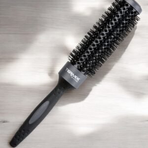 La Brosse Ronde XL Termix–Diamètre 60, dotée d’un design noir avec un manche texturé et des poils denses, repose sur une surface en bois clair, magnifiquement éclairée par la lumière naturelle.