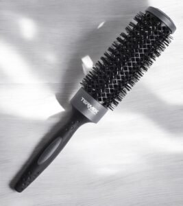 Une Brosse Ronde XL Termix–Diamètre 37 noire, dotée d'un long manche et de poils denses, repose sur une surface texturée gris clair. La brosse projette des ombres douces, avec son nom de marque imprimé près du manche.