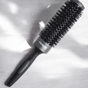 Une Brosse Ronde XL Termix–Diamètre 37 noire, dotée d'un long manche et de poils denses, repose sur une surface texturée gris clair. La brosse projette des ombres douces, avec son nom de marque imprimé près du manche.