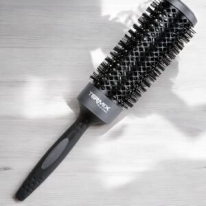 Une brosse à cheveux noire Brosse Ronde XL Termix - Diamètre 43 avec un corps et des poils ventilés repose sur une surface en bois clair. Le manche est doté d'une prise texturée et le nom de la marque « Termix » est imprimé sur le corps.