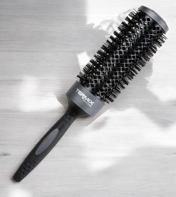 Une brosse à cheveux noire Brosse Ronde XL Termix - Diamètre 43 avec un corps et des poils ventilés repose sur une surface en bois clair. Le manche est doté d'une prise texturée et le nom de la marque « Termix » est imprimé sur le corps.