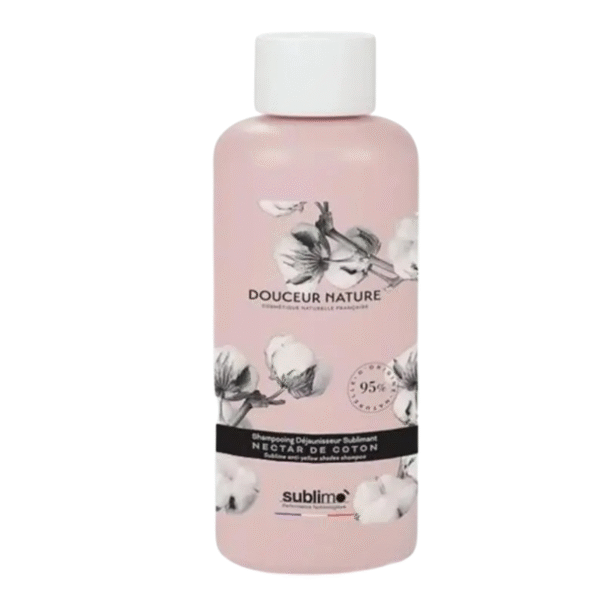 Un flacon rose de 250 ml de Shampooing Douceur Nectar de Coton-Déjaunisseur de Sublimo présente des illustrations de cotonniers, un bouchon blanc et une étiquette inférieure noire, offrant une expérience de shampooing douce et énergisante.
