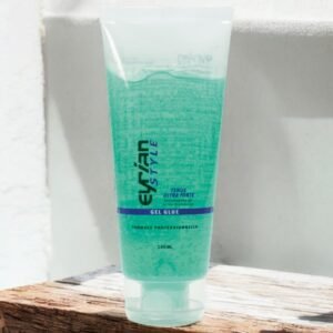 Un tube translucide de colle gel Evr'An Style est posé sur une surface en bois. Le tube contient 100 ml de produit, avec les inscriptions « Tenue Ultra Forte » et « Formule Professionnelle » visibles sur le devant. Le gel à l'intérieur apparaît vert clair.