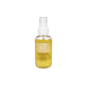 Un flacon transparent de 90 ml d'Huile sèche ultra illuminatrice-ENAYA avec une pompe blanche, un liquide jaune, un texte doré et des motifs botaniques blancs sur l'étiquette, présentés sur un fond blanc uni.