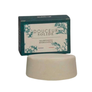 Une barre de Shampoing Solide Hydratation-Sublimo-Douceur -65g repose devant sa boîte, étiquetée « DOUCEUR SOLIDE » et « SHAMPOOING HYDRATATION », avec d'élégantes illustrations botaniques.