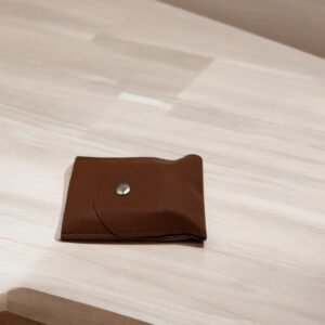 Le Set onglerie Marron, une pochette compacte en cuir marron avec fermeture à bouton, repose sur une surface en bois clair.