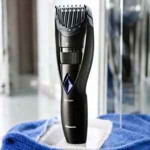 La tondeuse à barbe électrique noire ER-GB37-Panasonic est dotée d'un protège-barbe réglable et repose sur une serviette bleue pliée. Elle est dotée d'une molette pour régler la longueur et présente un design élégant et moderne.