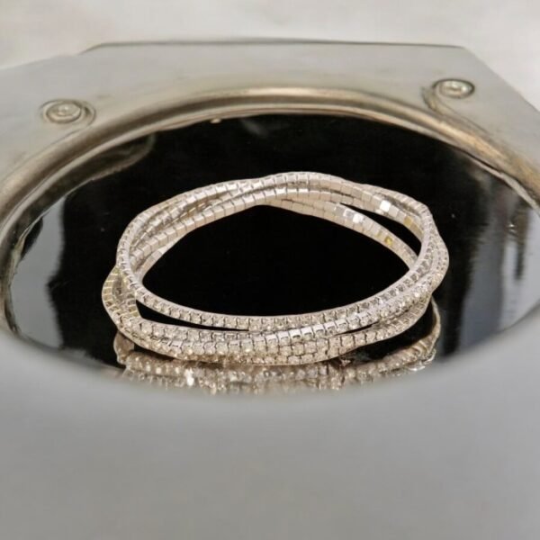 Deux « Bracelet élastique en métal et strass », présentant un superbe motif de maillons carrés, sont disposés de manière artistique dans un style d'accumulation chic sur une surface noire réfléchissante, entourée d'une élégante bordure métallique.