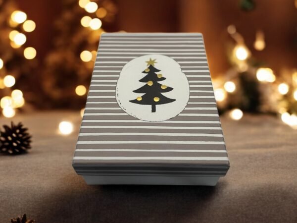 La « Boîte Cadeau - Rectangulaire - Noël - Sapin noir » arbore des rayures grises et blanches avec une étiquette ovale qui met en valeur un motif de sapin de Noël noir minimaliste. L'ambiance est encore enrichie par des lumières chaudes et floues et un fond chaleureux et festif, renforçant l'atmosphère de Noël.