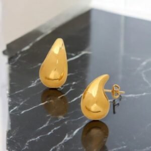 Une paire de boucles d'oreilles brillantes en or en forme de larme repose sur une surface en marbre noir brillant.