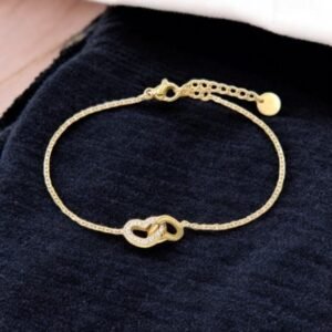 Bracelet en or avec un motif de coeurs entrelacés reposant sur une surface en tissu noir. Le bracelet est doté d'une chaîne délicate à maillons réglables et d'une petite breloque circulaire à l'extrémité.