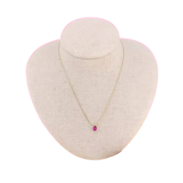 Le Collier court et son pendentif cristal forme goutte / Fushia, un collier délicat avec un pendentif en cristal en forme de goutte fuchsia, est présenté sur un buste à bijoux beige sur fond blanc.