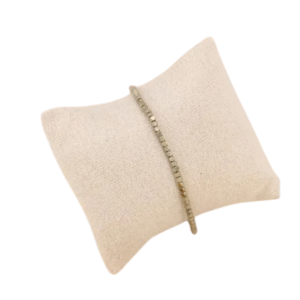 Le Bracelet à perles hématites forme cubes / Doré est présenté sur un coussin en tissu beige clair sur fond blanc.