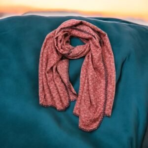 Une écharpe chinée longue à carreaux / Bleu foncé est artistiquement disposée sur un fond de tissu bleu sarcelle doux, sur fond de ciel de coucher de soleil flou.