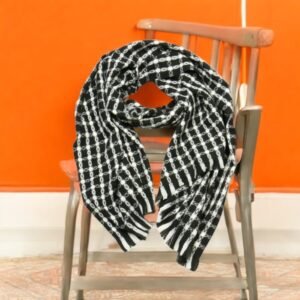 Une écharpe à motifs noirs et blancs drapée sur le dossier d'une chaise en bois. L'arrière-plan présente un mur orange et un sol à motifs.