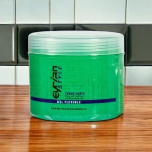 Un pot de gel capillaire « Gel flexible-Tenue Forte-Eyrian-Style », de couleur verte vibrante et d'un format de 500 ml, est posé sur une surface en bois. En arrière-plan, un mur carrelé ajoute une touche élégante, mettant en valeur la présentation épurée du produit.