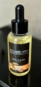 Un flacon de 50 ml d'Huile de barbe parfumée-Mangue Suave- Défi Pour homme est doté d'un bouchon compte-gouttes noir et d'une étiquette accrocheuse qui met en valeur ses éléments séduisants de mangue et de raisin. Positionnée sur une surface sombre réfléchissante, cette huile à barbe nourrissante est idéale pour garder votre barbe soyeuse et merveilleusement parfumée.