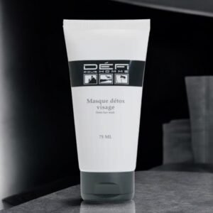 Un tube blanc de Masque Détox - Défi pour Homme repose sur une surface grise réfléchissante, sur un fond sombre aux tons gris subtils, soulignant son rôle de soin détoxifiant visage purifiant pour hommes.