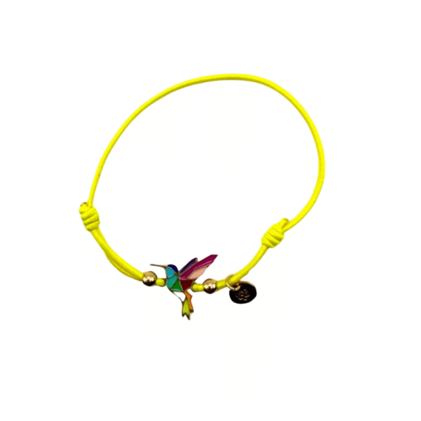 Un bracelet en cordon jaune vif, "Bracelet acier inoxydable laqué argent colibri/Jaune", comporte une breloque colibri géométrique colorée en acier inoxydable émaillé, deux petites perles en or et une étiquette ronde en or sur un fond blanc uni.
