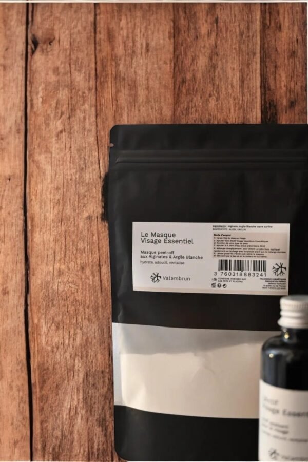 Gros plan d'un emballage noir et blanc étiqueté « Masque Peel Off Essentiel (3) 70G - Saly Cosmétiques » sur une surface en bois, avec une petite bouteille sombre partiellement visible au premier plan, suggérant davantage de produits de soins de la peau.