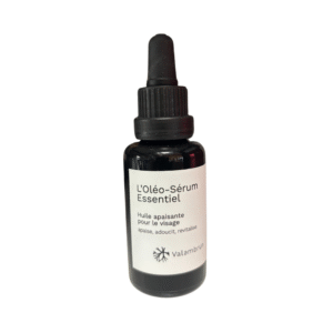 Un flacon compte-gouttes en verre foncé étiqueté « Oléo Sérum Essentiel 30 ml-Saly Cosmétiques » comporte un bouchon compte-gouttes noir et une étiquette blanche, le décrivant comme une huile apaisante pour le visage.