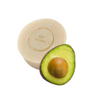 Une barre ronde de savon douceur d'avocat de 120 g de Saly Cosmétiques, arborant un logo en relief, est placée derrière un avocat coupé en deux avec noyau visible et chair verte sur fond blanc.
