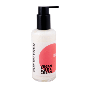Un flacon blanc avec une pompe noire, étiqueté « Crème Vegan Curl Définition Boucles-150Ml-Cut by Fred », présente un motif de cercle rose sur le devant.