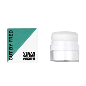 Une boîte blanche et verte étiquetée « Shampooing sec Vegan Volume Powder-10g- Cut by Fred » se trouve à côté d'un récipient transparent avec un applicateur éponge blanc sur un fond blanc uni, idéal pour les personnes en quête d'hydratation capillaire végétalienne.