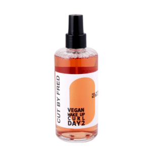 Le spray Vegan Wake up Curl Jour 2 - 200 ml de Cut by Fred est un flacon transparent contenant un liquide orange, un embout vaporisateur noir et une étiquette blanche ornée d'une orange. C'est un raviveur de boucles vegan pour les cheveux du deuxième jour.