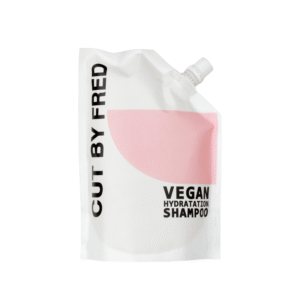 Une pochette de recharge blanche de 520 ml avec un design en demi-cercle rose et un bouchon à vis en haut à droite, étiqueté « Recharge Shampooing Hydratant-Vegan-Cut by Fred ».