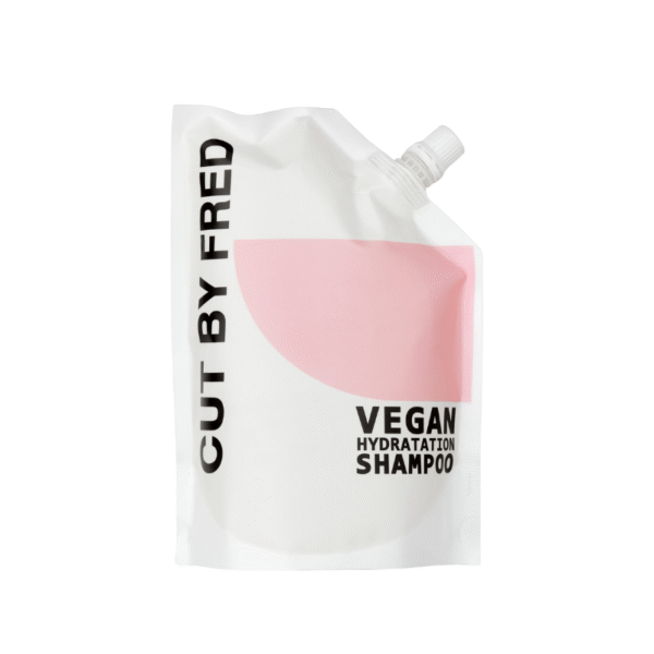 Une pochette de recharge blanche de 520 ml avec un design en demi-cercle rose et un bouchon à vis en haut à droite, étiqueté « Recharge Shampooing Hydratant-Vegan-Cut by Fred ».
