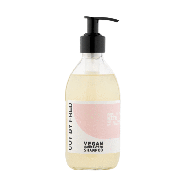 Un flacon pompe transparent de Shampooing Hydratant -Vegan-290ml de Cut by Fred, doté d'une étiquette rose clair et blanche avec texte noir et distributeur, rempli de liquide jaune pâle - votre soin capillaire hydratant végétalien essentiel.