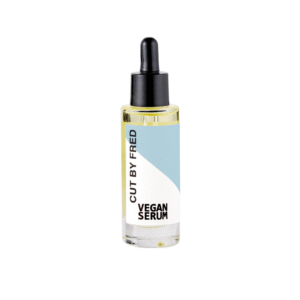 Un flacon compte-gouttes en verre transparent avec un bouchon noir et une étiquette bleu-blanc portant l'inscription « Vegan Serum-nourrissant-30ML - Cut by Fred », contenant un liquide jaune clair, idéal comme sérum de soin capillaire végétalien nourrissant.